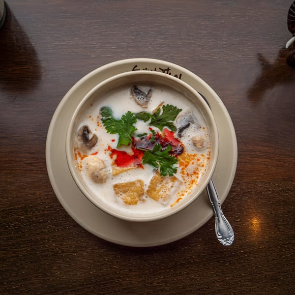 Creamy Thai soup with mushrooms, tofu, cilantro, and chili oil on a wooden table.