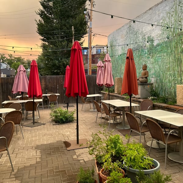 Outdoor patio at Swing Thai Tennyson with red umbrellas, tables, chairs, and a Buddha statue against a mural.