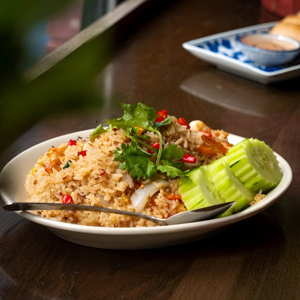 Thai fried rice with shrimp, red peppers, cilantro, and cucumber slices on a white plate.