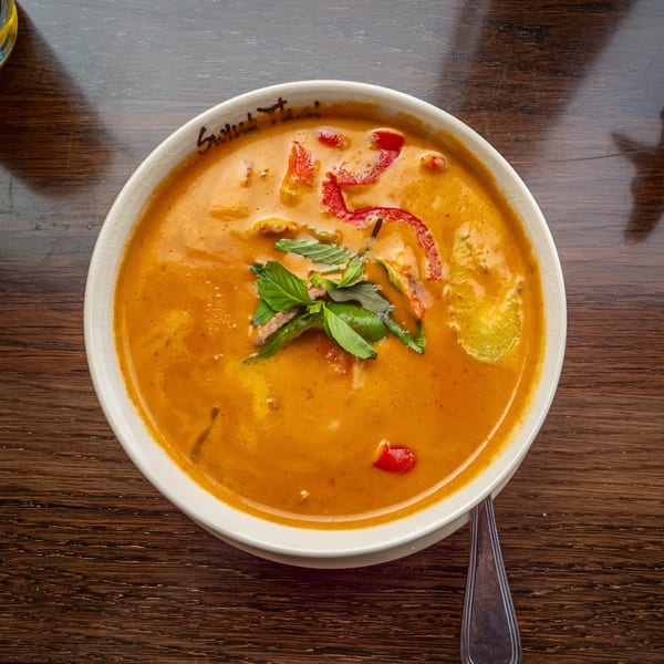 Swing Thai's red curry with basil and red peppers in a white bowl on a wooden table.