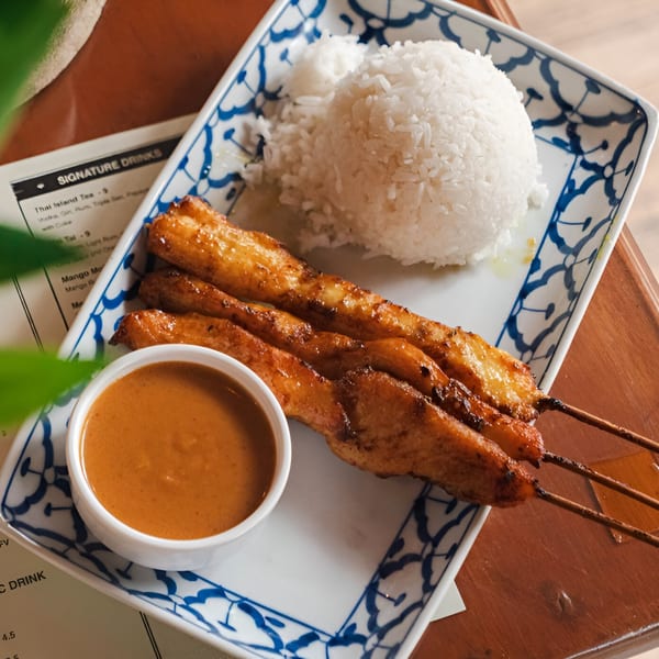 Chicken satay skewers with peanut sauce and white rice on a blue and white patterned plate.