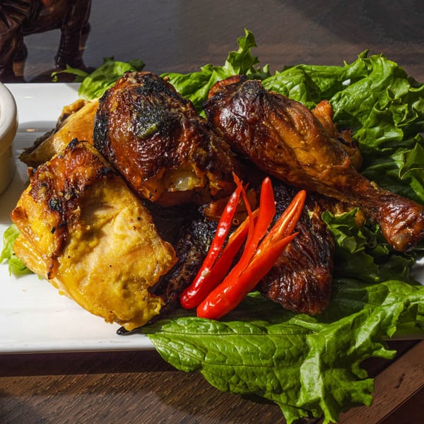 Grilled chicken pieces with red chili peppers and lettuce on a white plate at Swing Thai Tennyson.