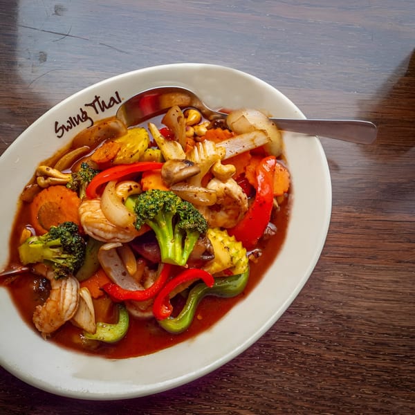 A white oval plate of Swing Thai stir-fry with shrimp, broccoli, bell peppers, and cashews.