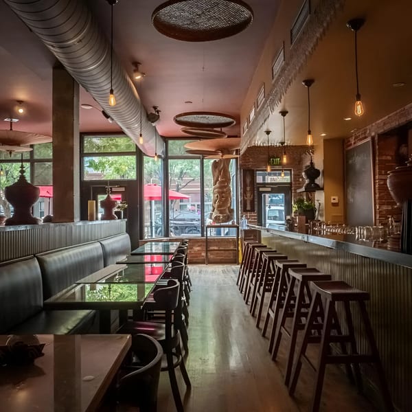 Interior of Swing Thai Tennyson, featuring a long bar with stools and booth seating with glass-top tables.