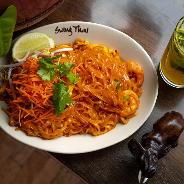 Swing Thai Tennyson's Pad Thai with shrimp, shredded carrots, cilantro, and lime, next to a drink.